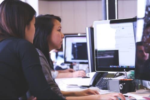 Photo of two women working at a computer, looking at the monitor.