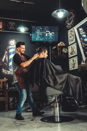 Owner in a modern, urban barbershop providing a hair cut to a client. Custom software tracks the specific details you need to interact with your clients best.