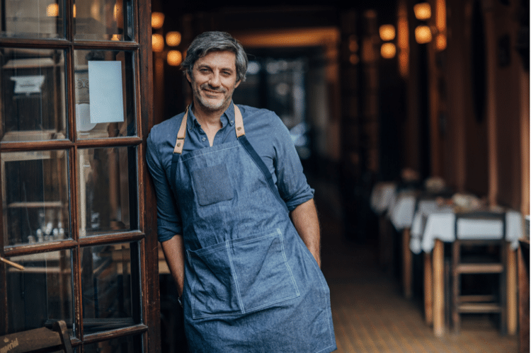 Restaurant owner leaning against the open door of his casual, upscale restaurant