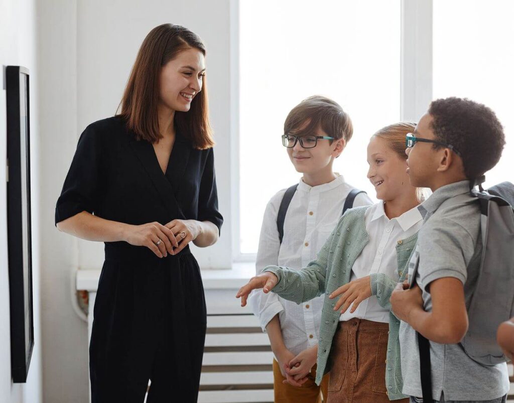 Photo of woman guiding a group of children on a tour of a museum or art gallery.