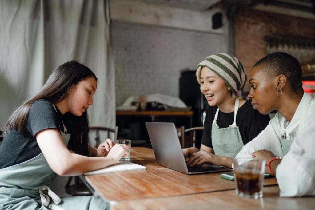 Coworkers sitting at a table, one with a laptop, one with a notepad, enjoying a discussion. Perhaps they are discussing FileMaker.