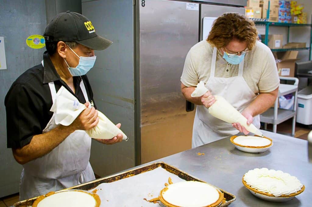 Image from the television series Undercover Boss, showing a boss in disguise learning how to make pies alongside his employee, to stay relevant within his operation.