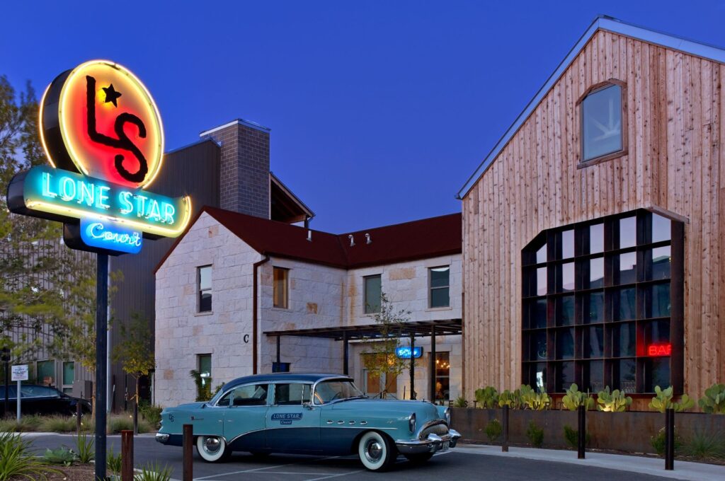 Photograph of Lone Star Court, a hotel in Austin, Texas, with brightly lit neon sign and teal vintage car out front.