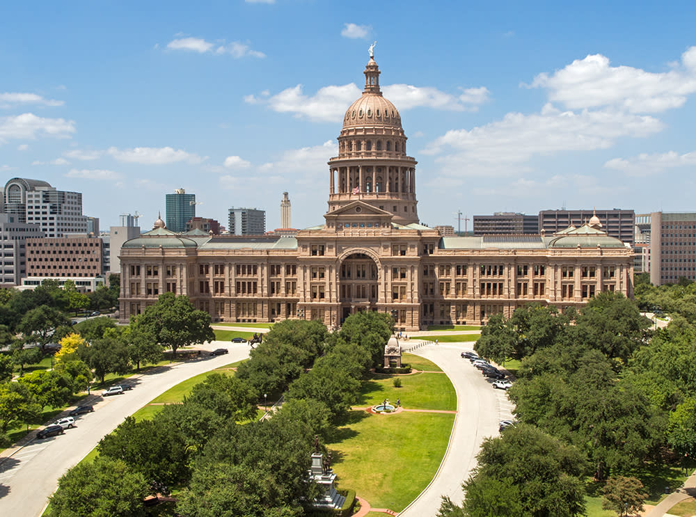 Photograph of the exterior of the Capitol building in Austin, Texas, with landscaping in the foreground and city skyline behind.