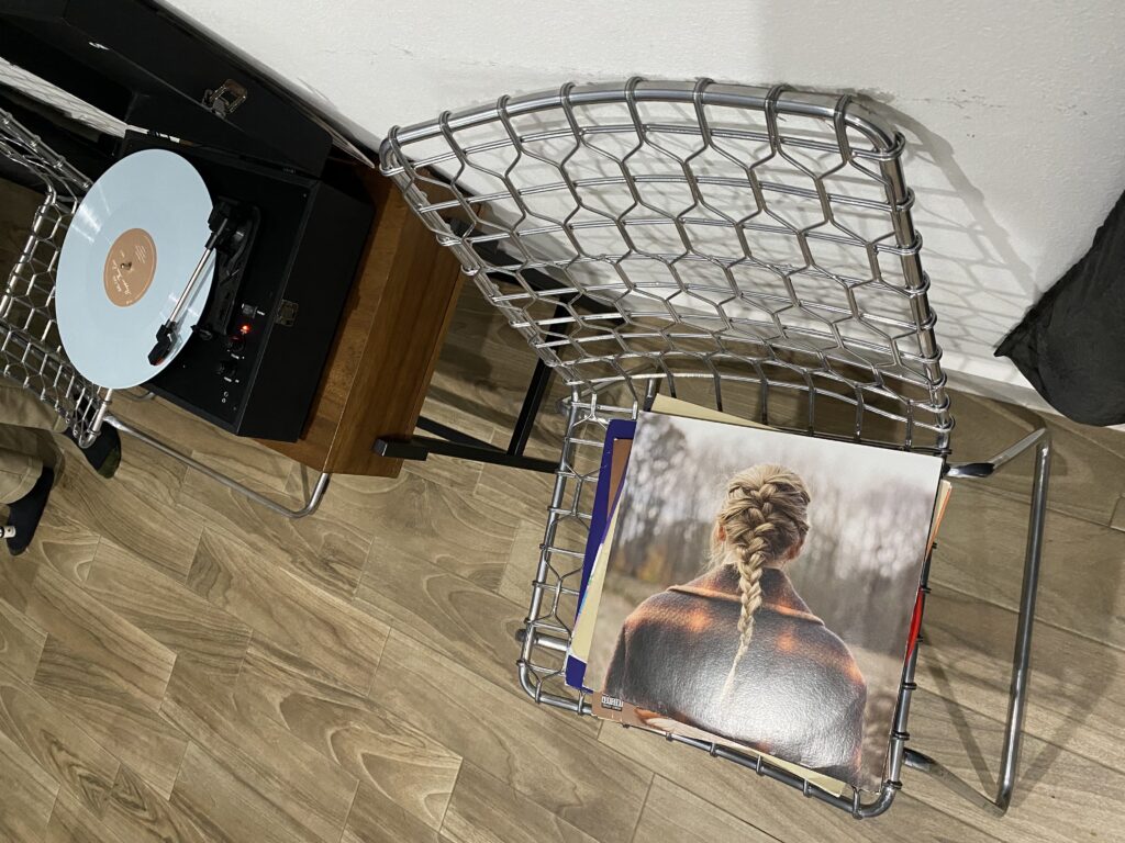 Overhead photo of metal chairs, a record player, and a stack of vinyl albums, with a Taylor Swift album on top.