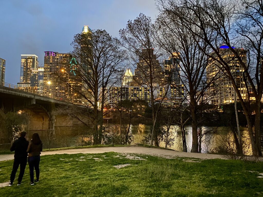 Photo of the Austin skyline at evening, as seen from a grassy area near one of the bat bridges.