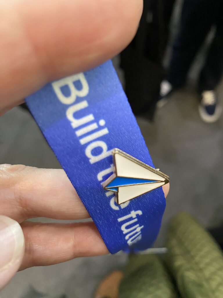 Up close photo of a Claris Engage 2024 conference lanyard, with a paper airplane pin attached.