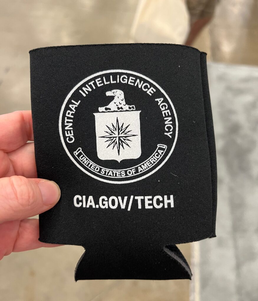A phot of Kate holding a black cup cozy, printed with the CIA logo. cia.gov/tech