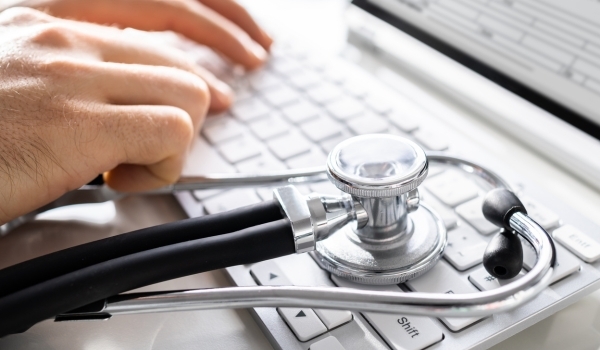 Two hands typing on a keyboard in the background with the focus being on a stethoscope laying on the keyboard in the foreground. Illustrating a company who upgraded to the latest version of FileMaker.