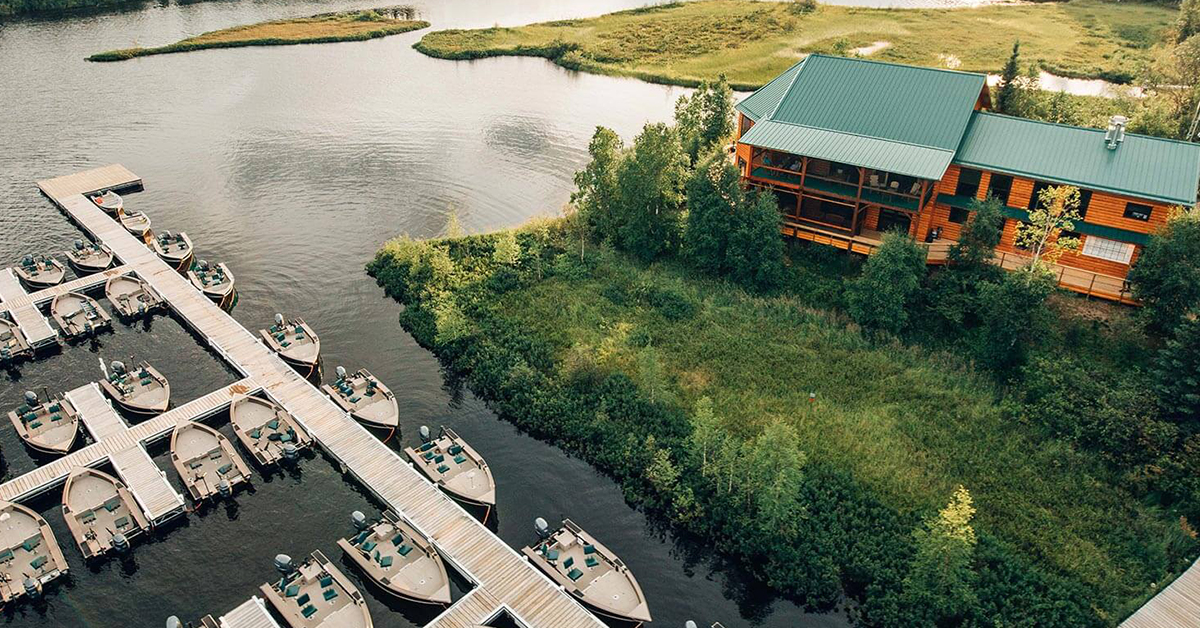 A lakeside doc with rows of boats on the left side of the screen and a lake house on the right
